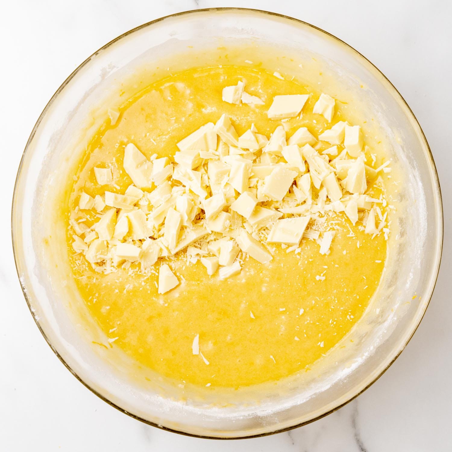 chopped white chocolate added to a yellow mixture for lemon brownies that is in a glass mixing bowl.