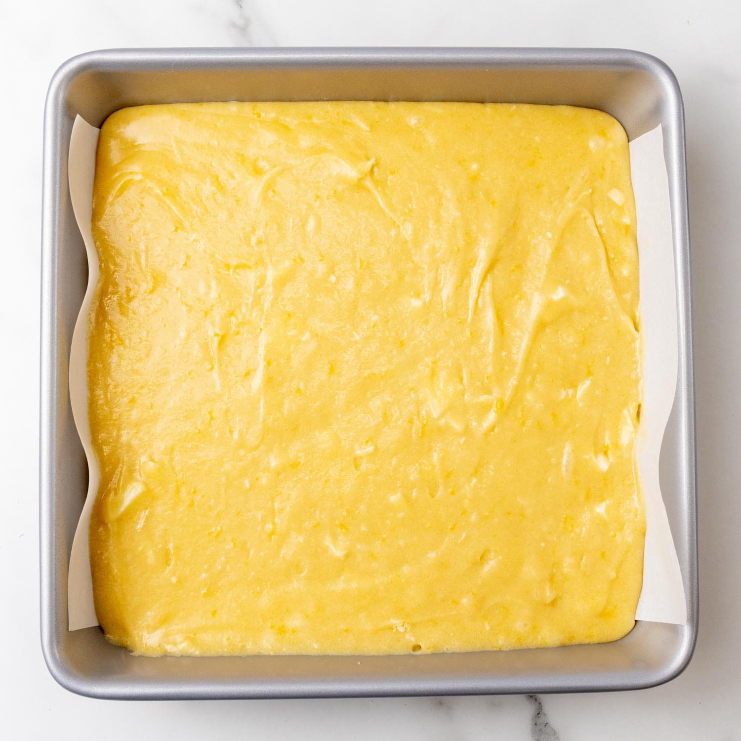 Lemon brownie batter in a square metal pan that is lined with parchment paper.