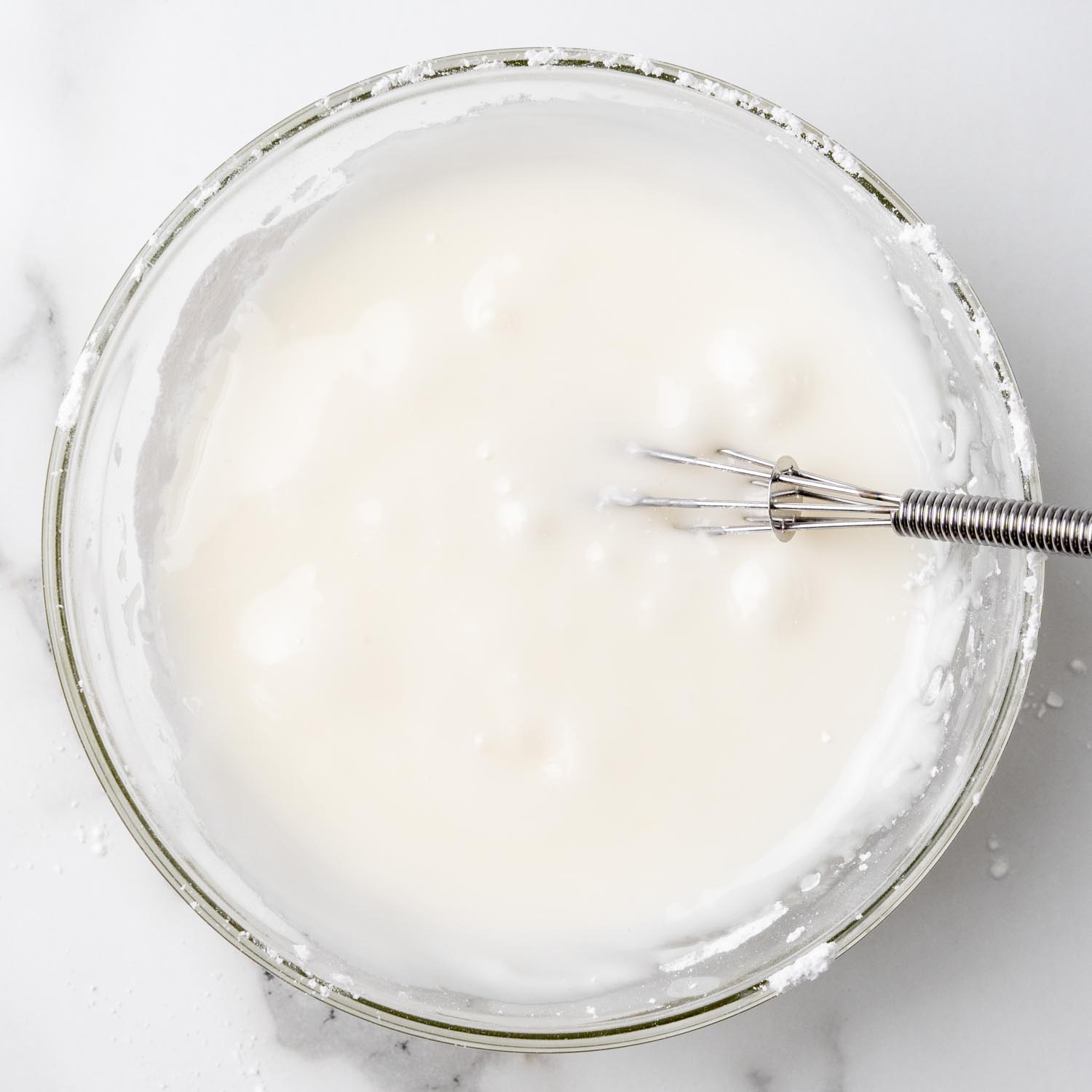 a glass bowl of icing with a whisk in it. 