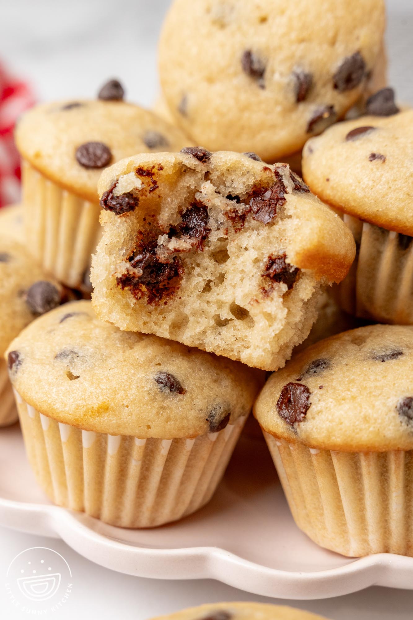 closeup of a platter of mini muffins. One has a bite taken to show the airy texture and chocolate chips inside.