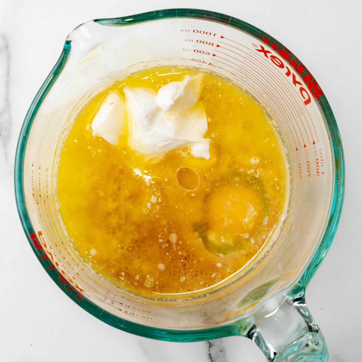 a glass measuring cup with oil, eggs, butter, and sour cream in it, viewed from overhead.