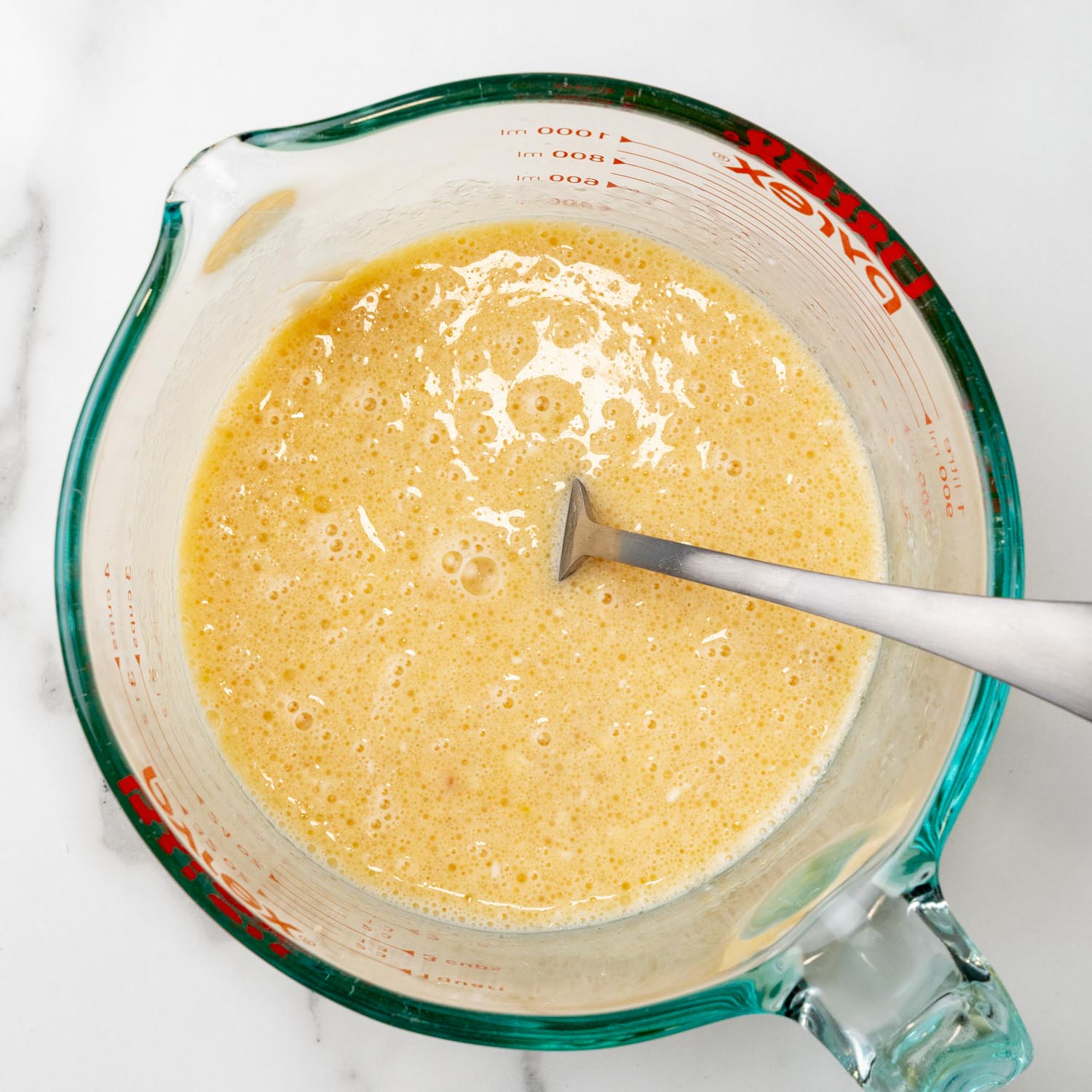 Wet ingredients for chocolate chip muffins mixed together inside a glass pyrex measuring cup with a metal fork.