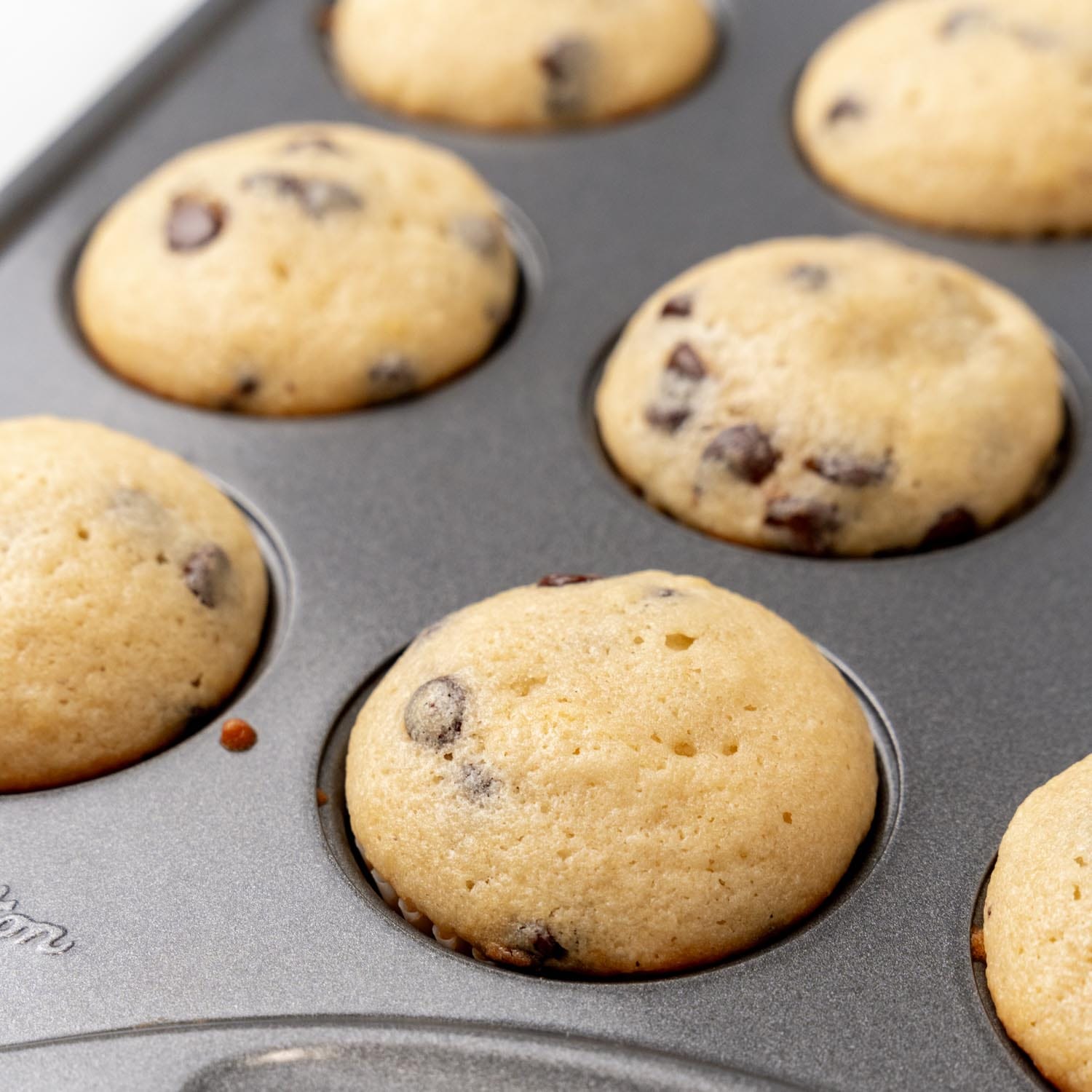 closeup of baked chocolate chip mini muffins in a metal muffin pan.