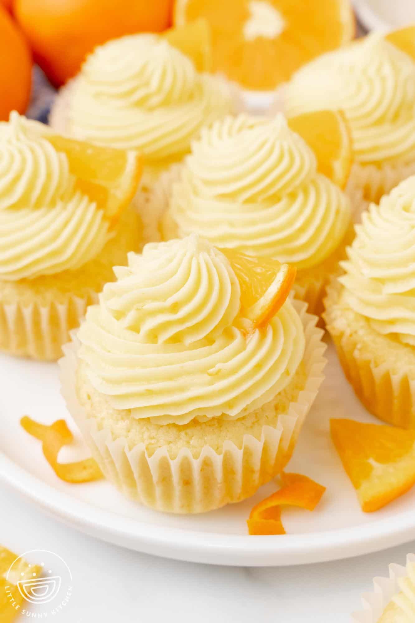 Orange cupcakes with orange zest buttercream on a plate, decorated with fresh orange wedges and zest curls.