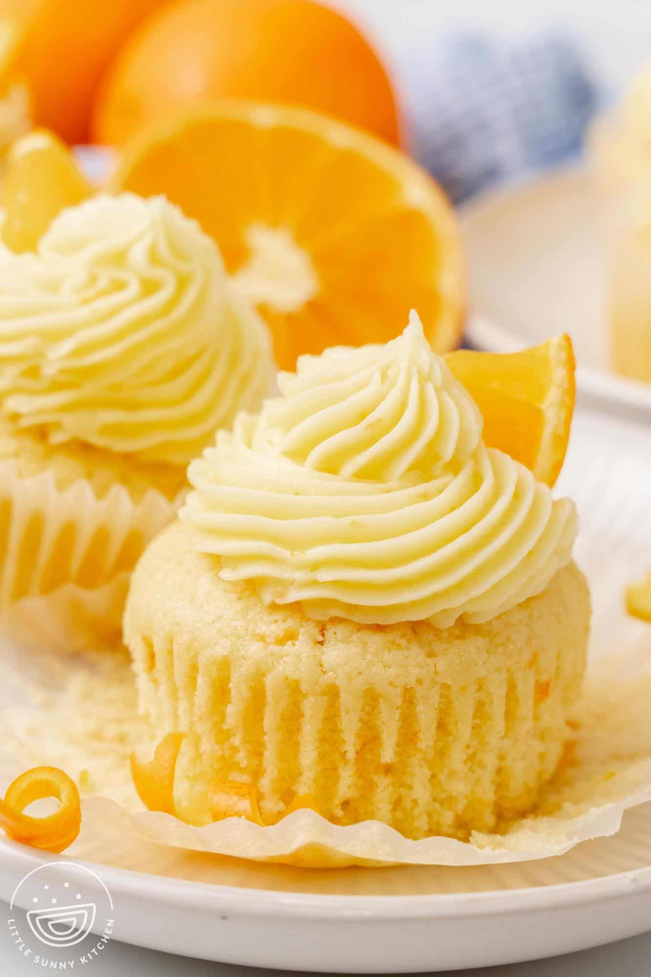 Orange cupcakes on a plate. The paper wrappers are pulled down.