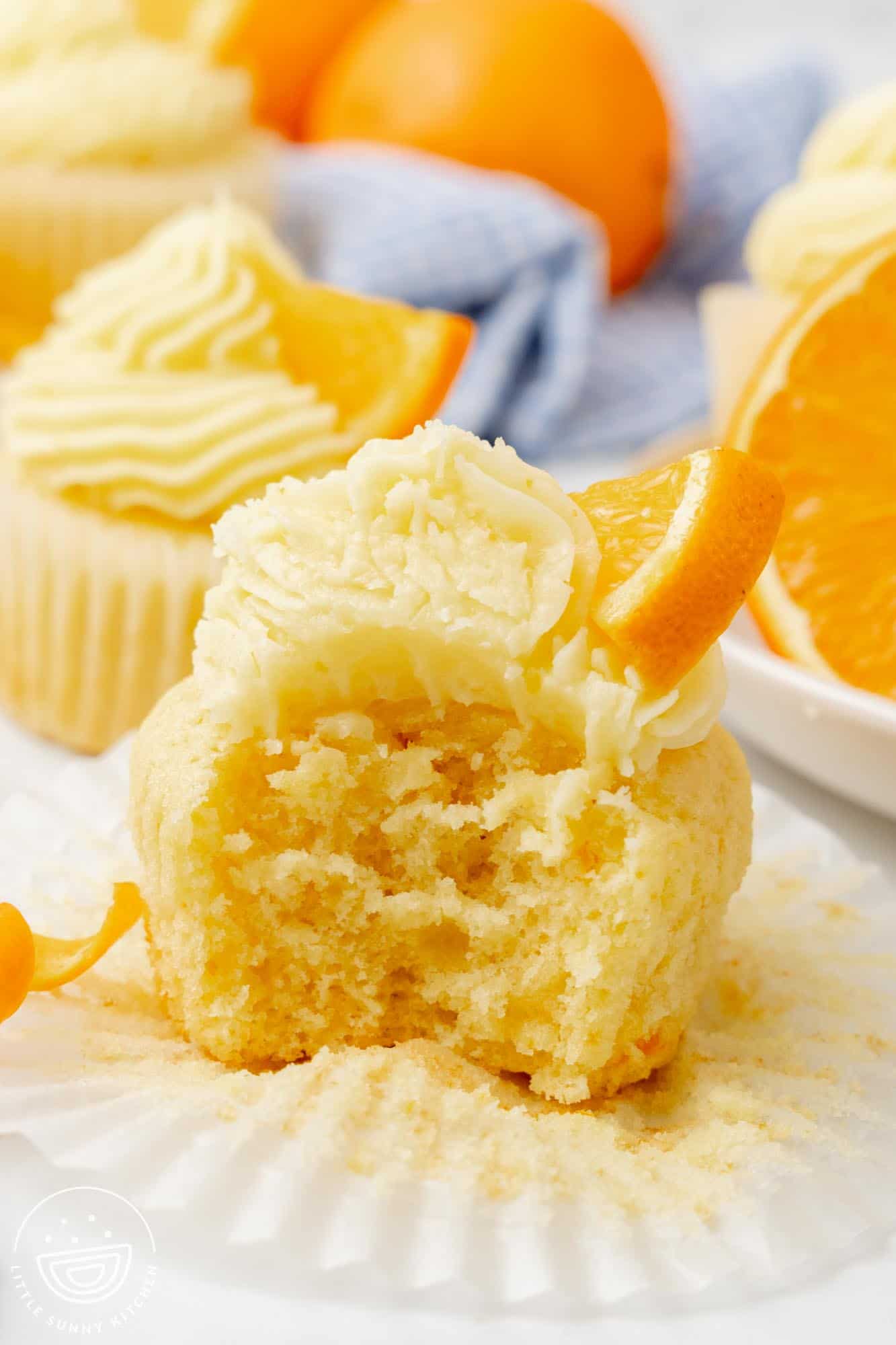 an orange cupcake with frosting. A bite has been taken to show the light, fluffy texture.