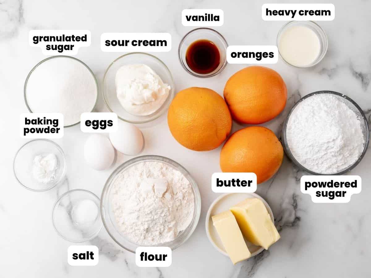 Three oranges, surrounded by small bowls of baking ingredients for making orange cupcakes.