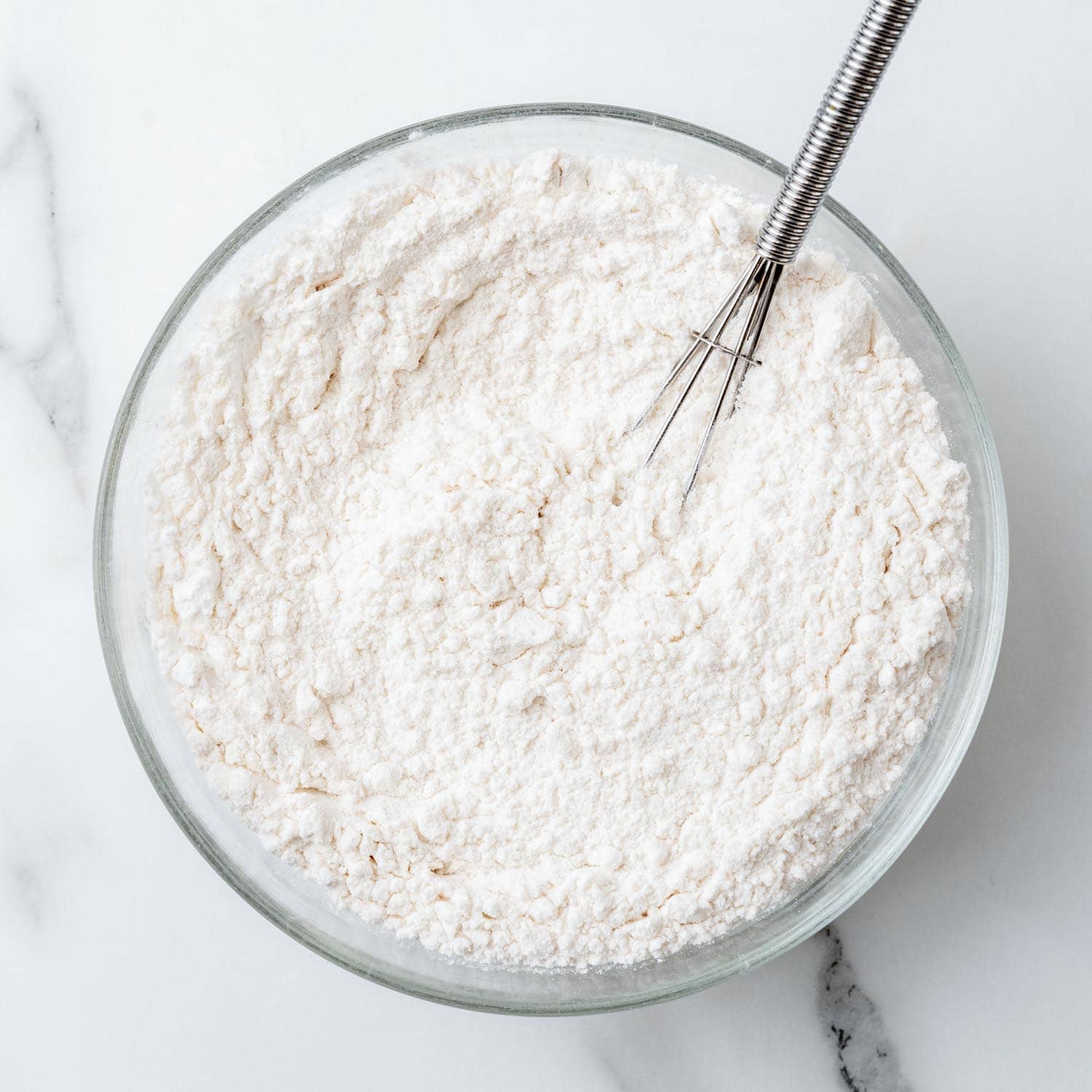 Flour in a glass bowl with a whisk.