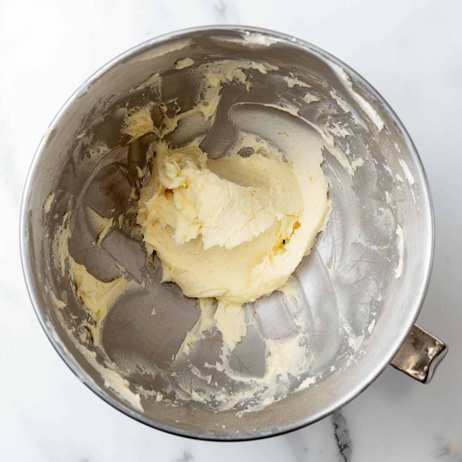 creamy orange frosting for cupcakes in a metal mixing bowl, viewed from overhead.