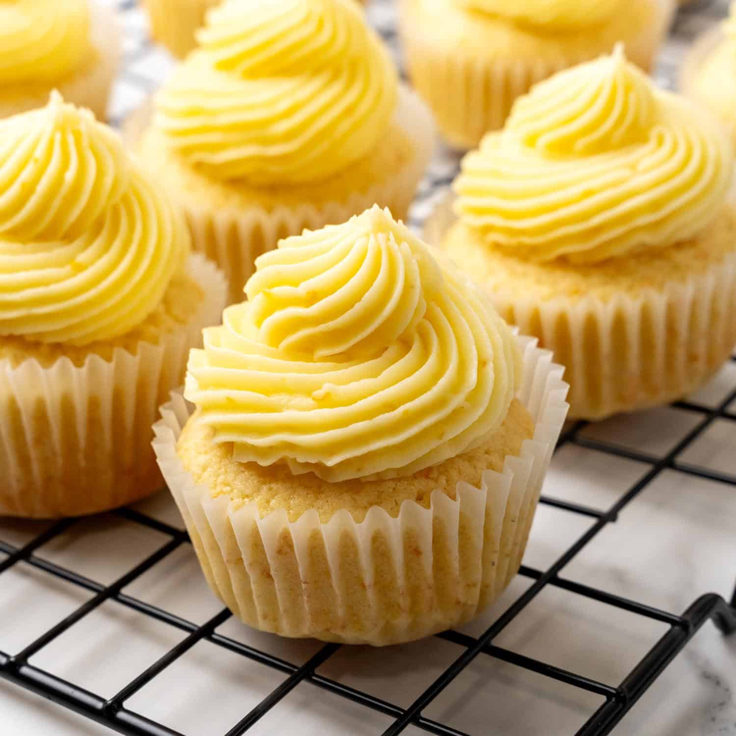 Cupcakes on a wire rack, topped with orange zest infused buttercream icing swirls.