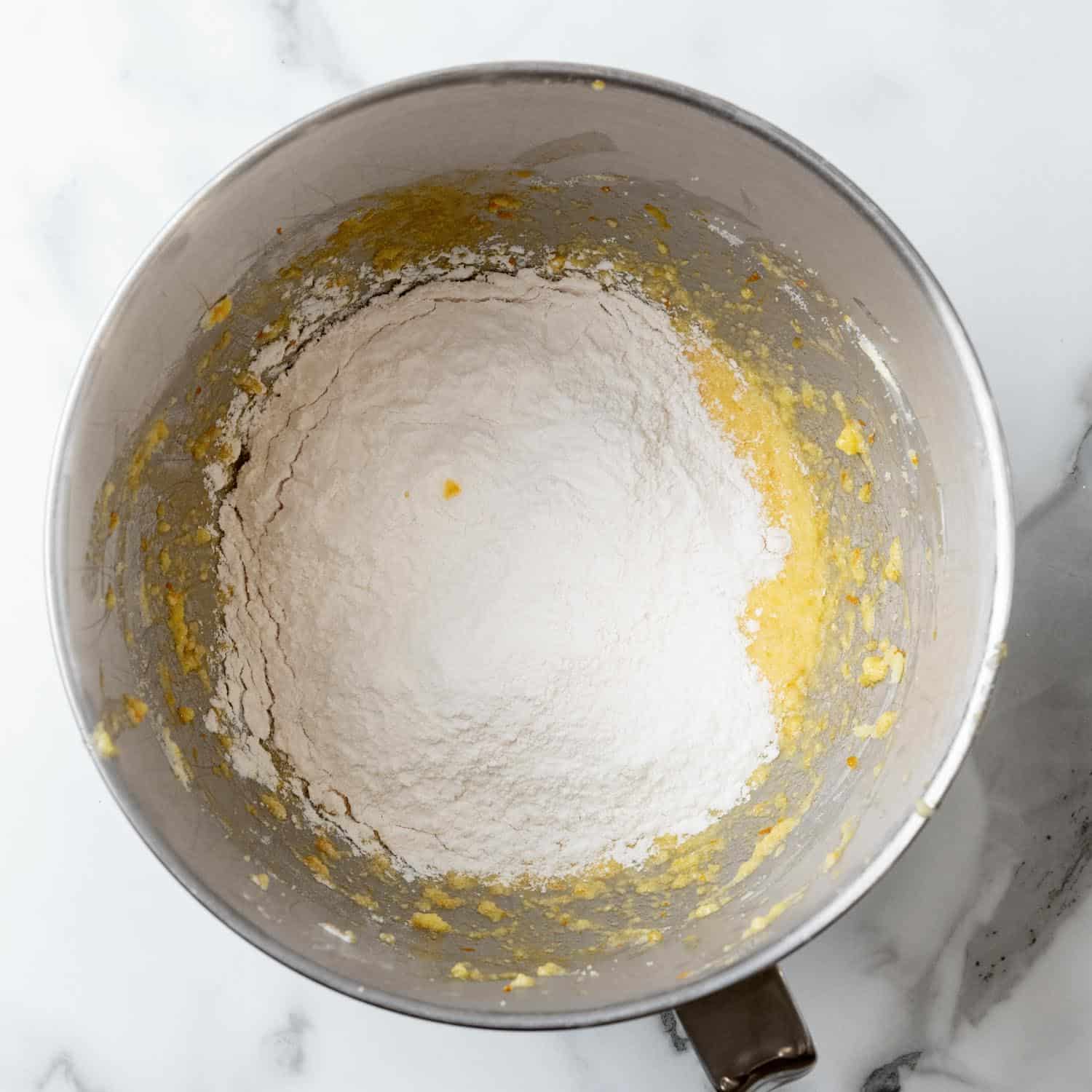 Dry ingredients added to wet ingredients for Orange cupcakes in a metal stand mixer bowl.