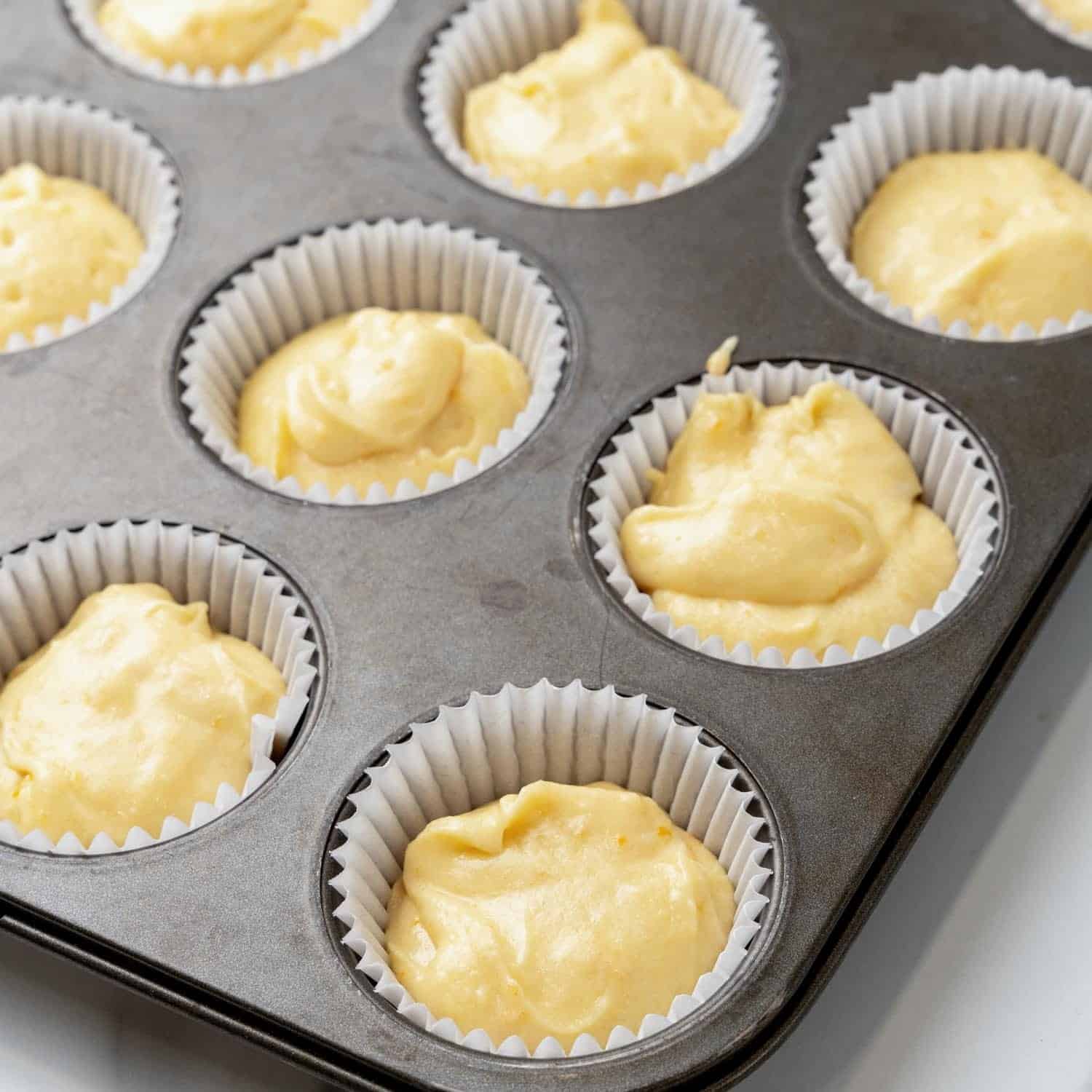 Cupcake batter in paper cups in a muffin pan.