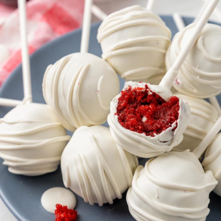 a plate of red velvet cake pops. one has been bitten to show the deep red moist cake inside.