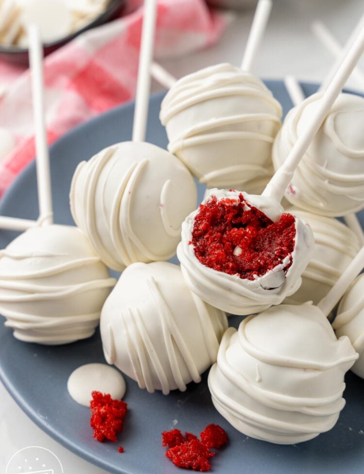 a plate of red velvet cake pops. one has been bitten to show the deep red moist cake inside.