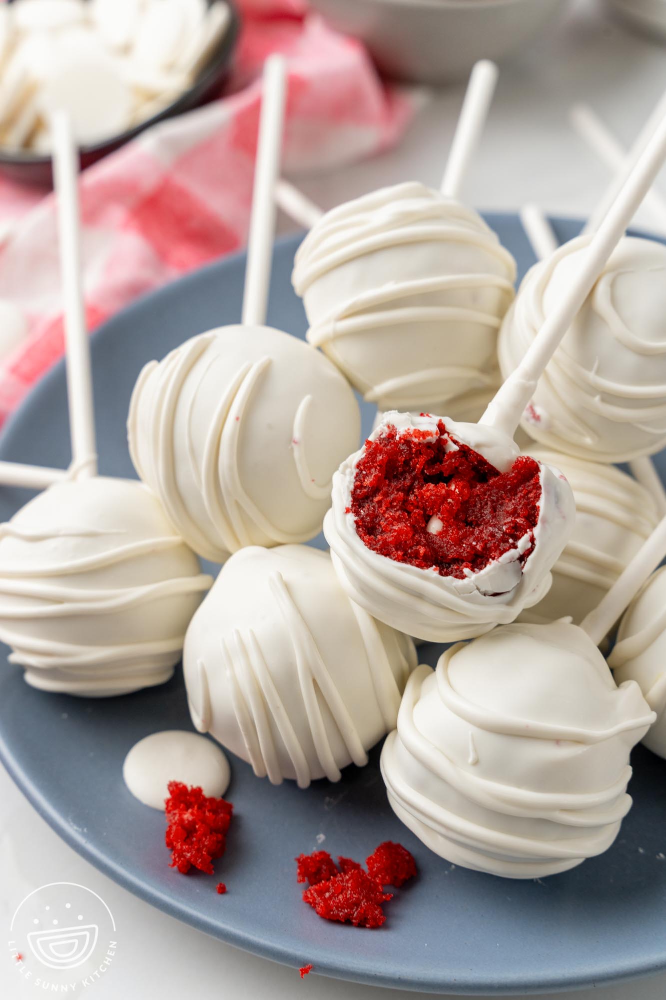 a plate of red velvet cake pops. one has been bitten to show the deep red moist cake inside.