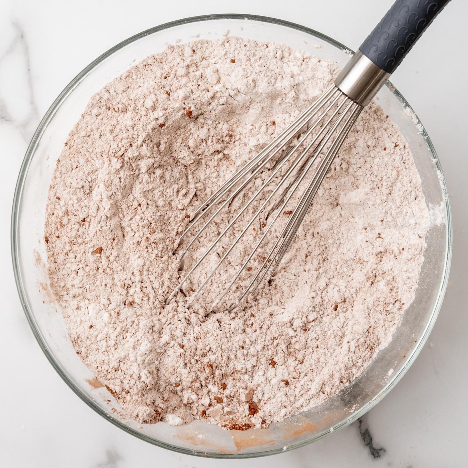 flour and cocoa powder whisked together in a glass bowl on a marble counter.