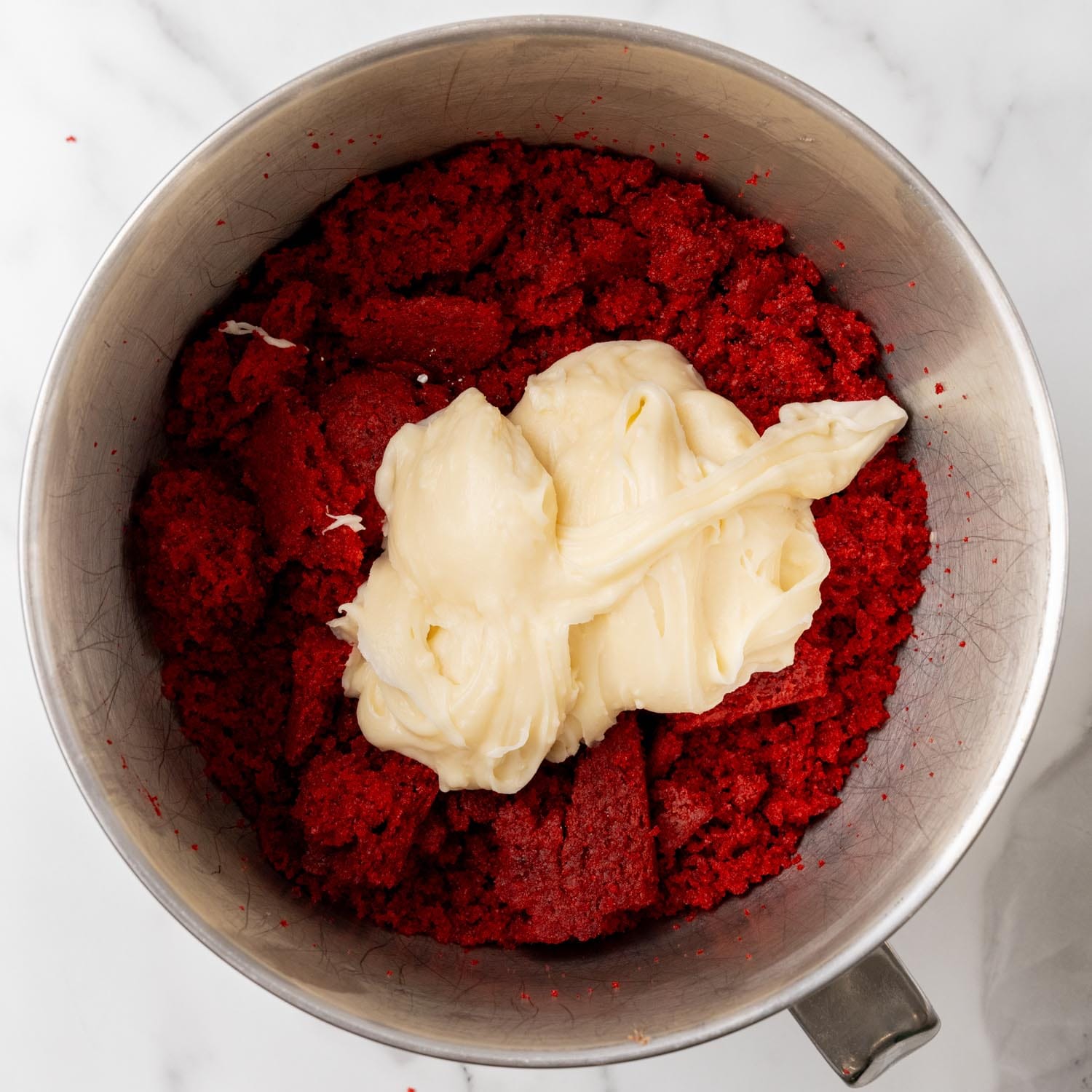 cream cheese frosting added to crumbled red velvet cake to make cake pops in a metal stand mixer bowl.