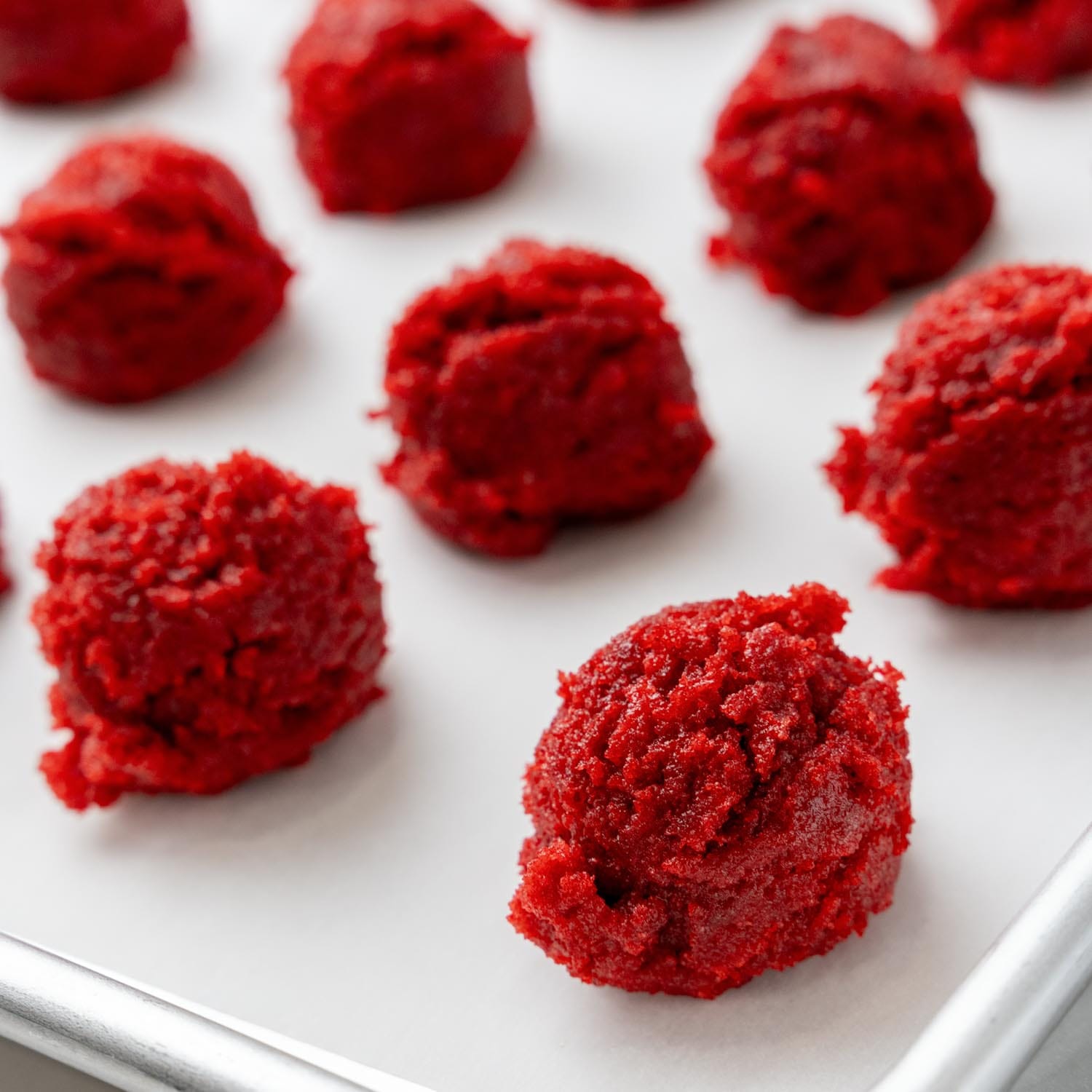 round scoops of red velvet cake pop dough on a parchment lined baking sheet.