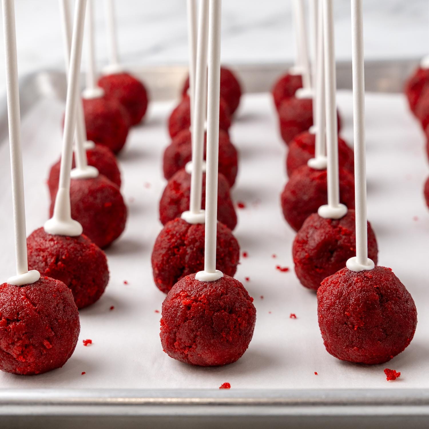 red velvet cake pops with sticks in them, uncoated, on a baking sheet.