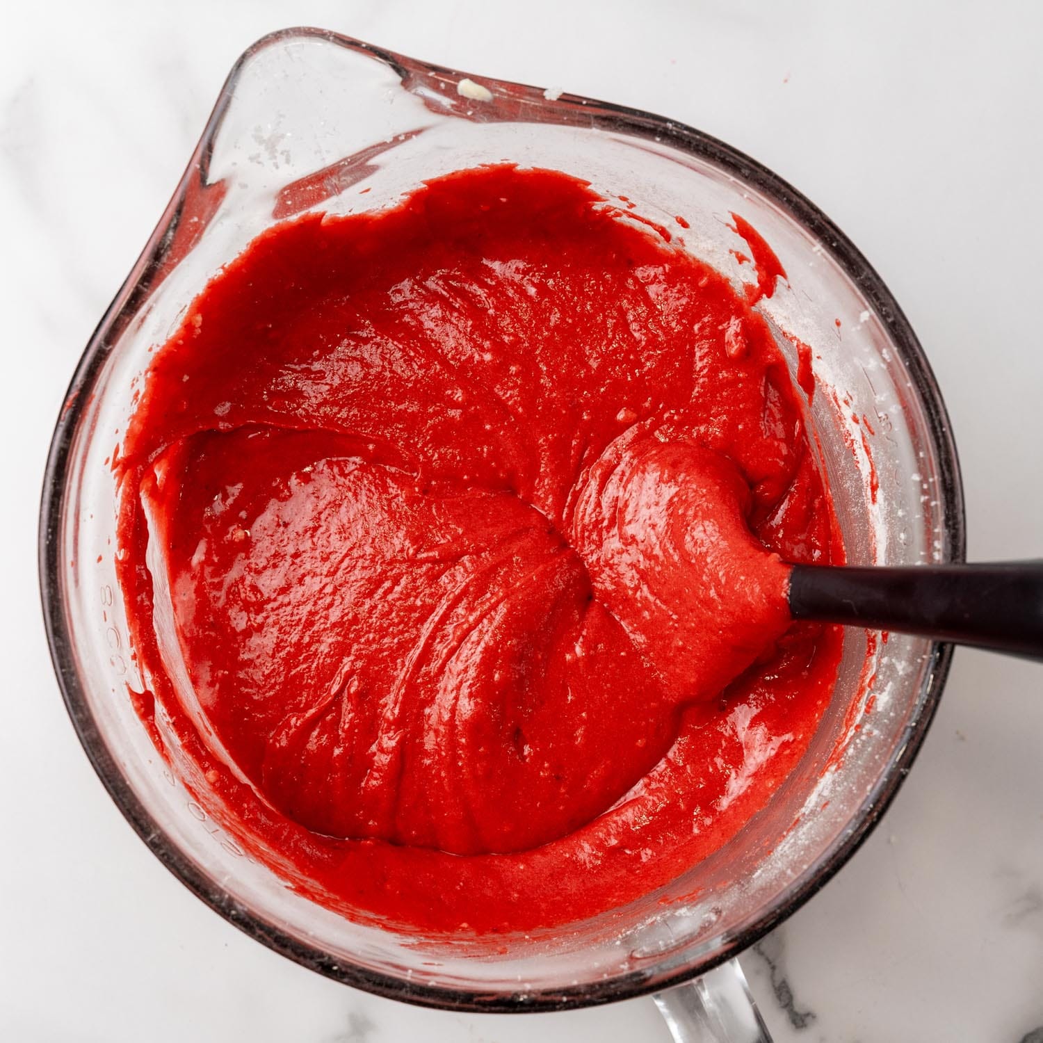 deep red velvet cake batter in a glass mixing bowl with a spout and handle.