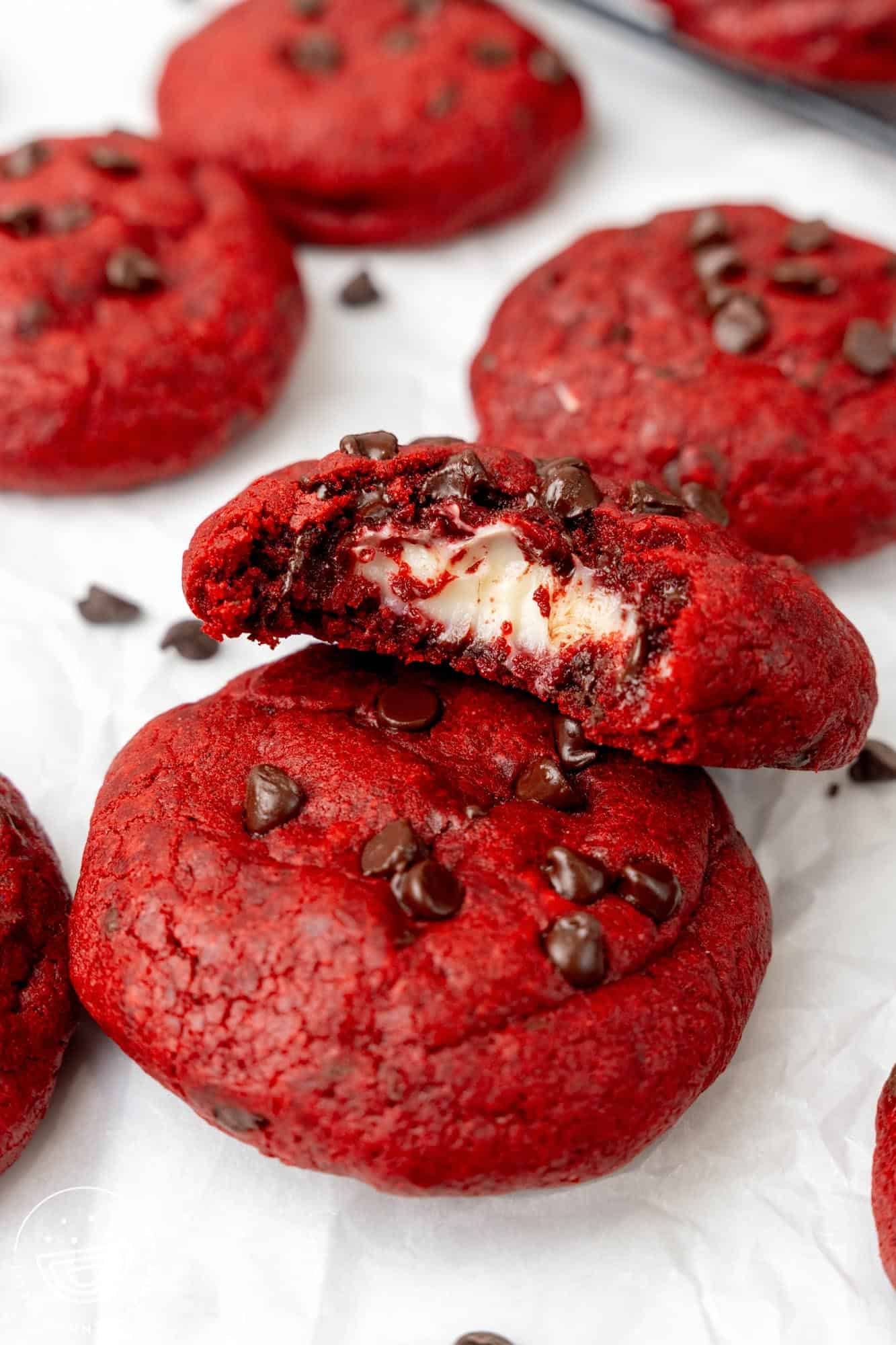 red velvet cream cheese cookies on parchment paper. One has a bite taken to show the filling inside.