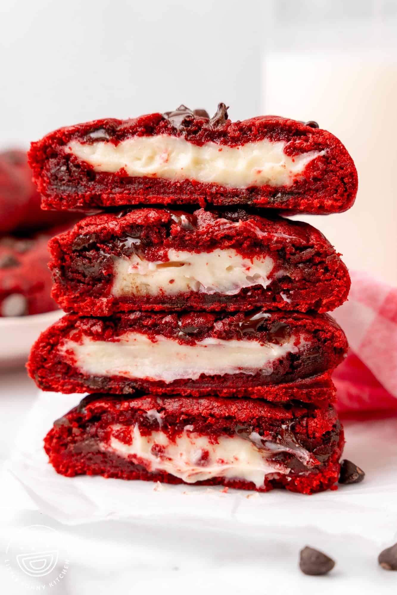 A stack of four red velvet stuffed cookies that have been cut in half to show the cream cheese filling.