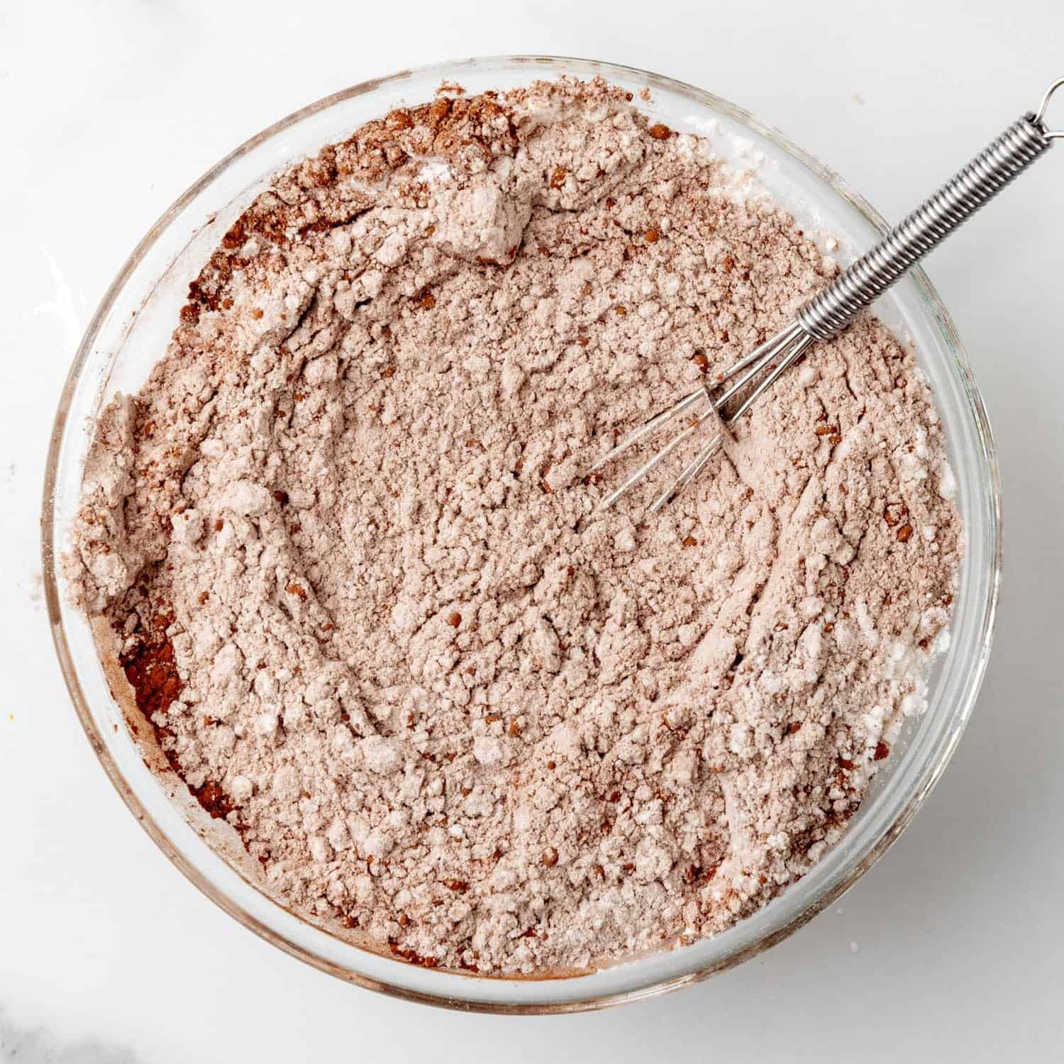 Dry ingredients including flour and cocoa powder, combined for red velvet cookie dough with a whisk.