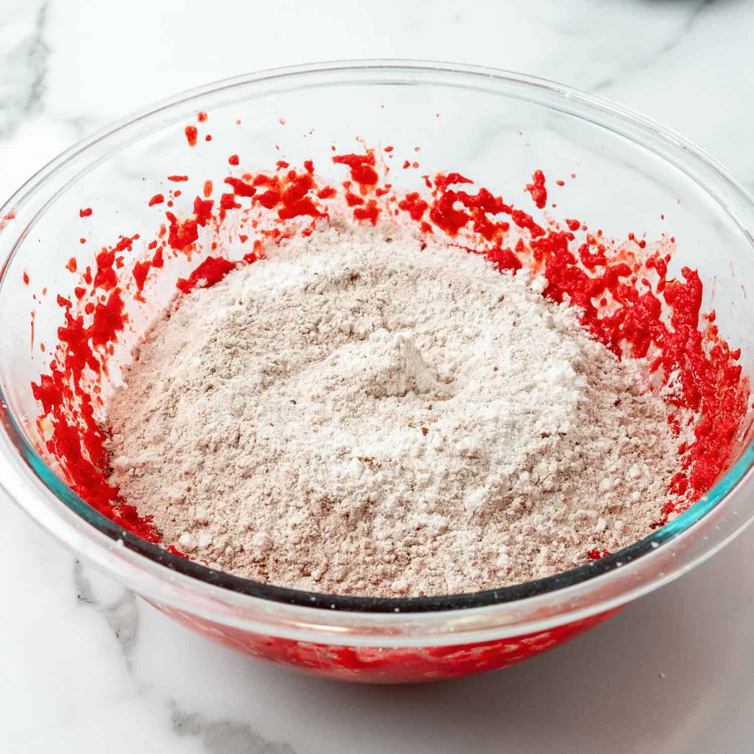 dry ingredients added to wet ingredients for red velvet cookies in a glass mixing bowl.