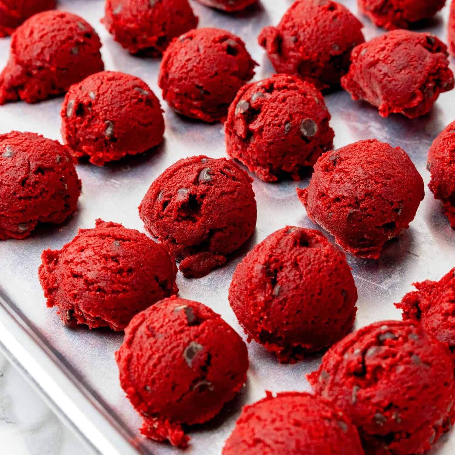 round scoops of chocolate chip red velvet cookie dough on a sheet pan