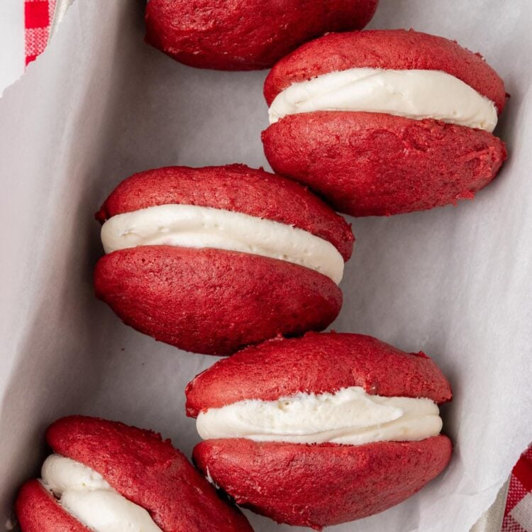 four red velvet whoopie pie sandwiches in a parchment lined baking pan.