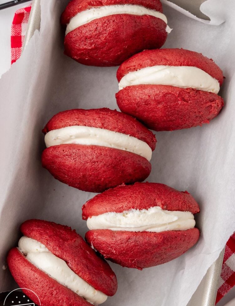 four red velvet whoopie pie sandwiches in a parchment lined baking pan.