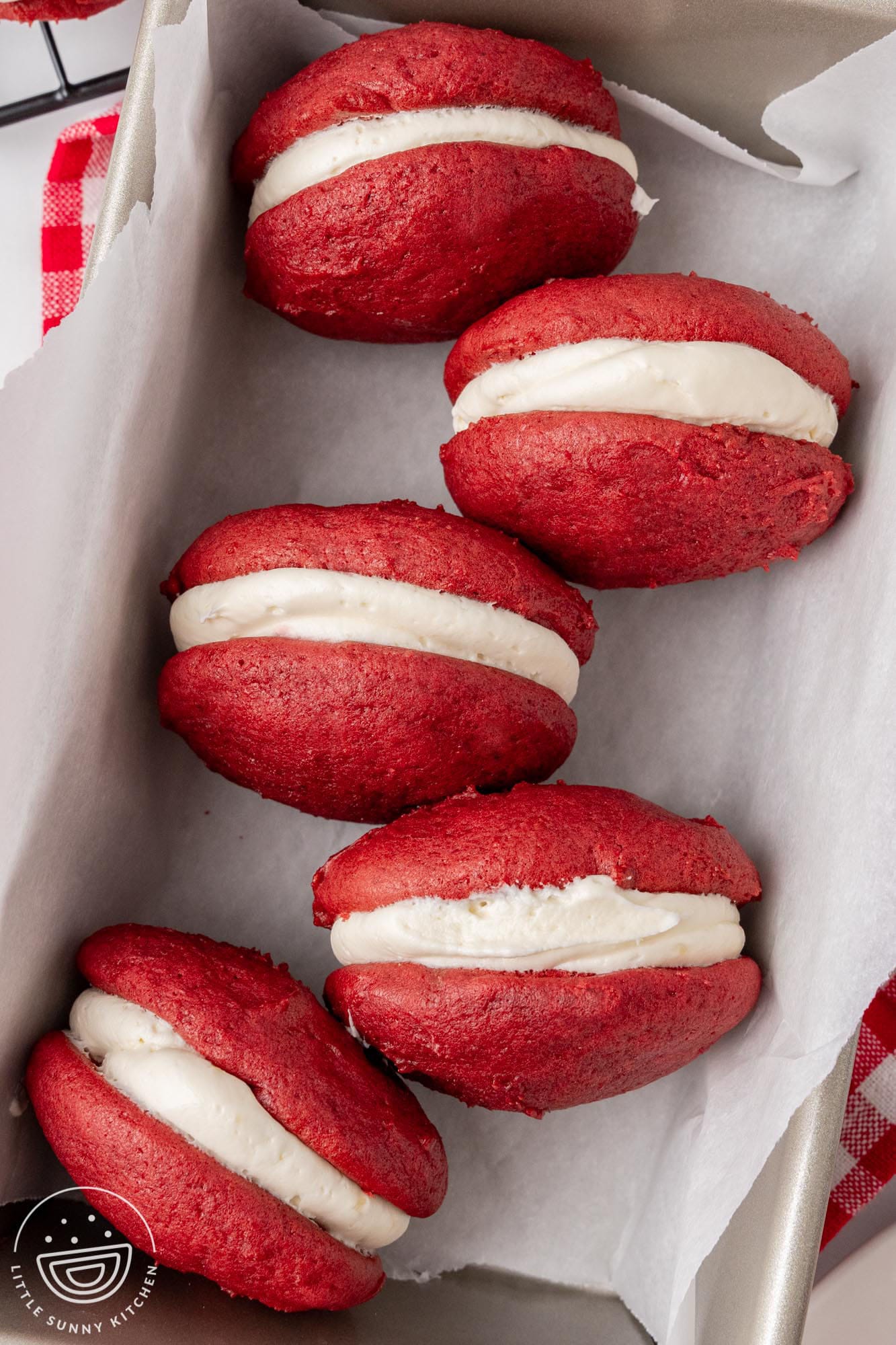 four red velvet whoopie pie sandwiches in a parchment lined baking pan.