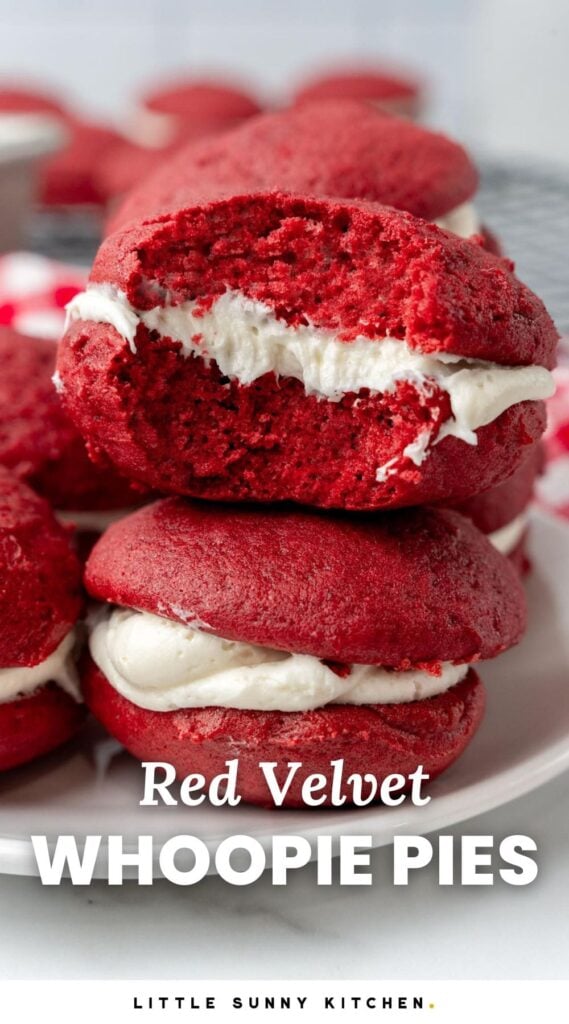 red velvet cake whoopie pies with cream cheese filling on a plate. One has a bite taken out. Text overlay at the bottom of the image says "Red Velvet Whoopie Pies"