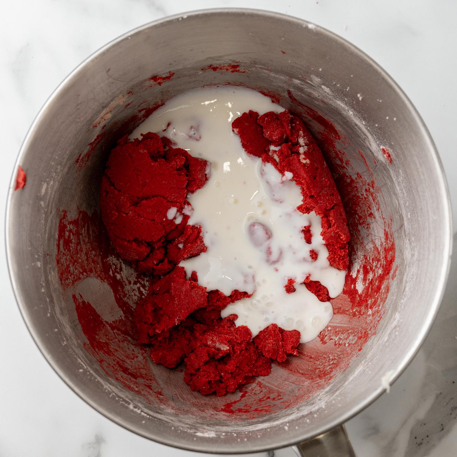 buttermilk added to red velvet cake batter for whoopie pies, in a metal mixing bowl.