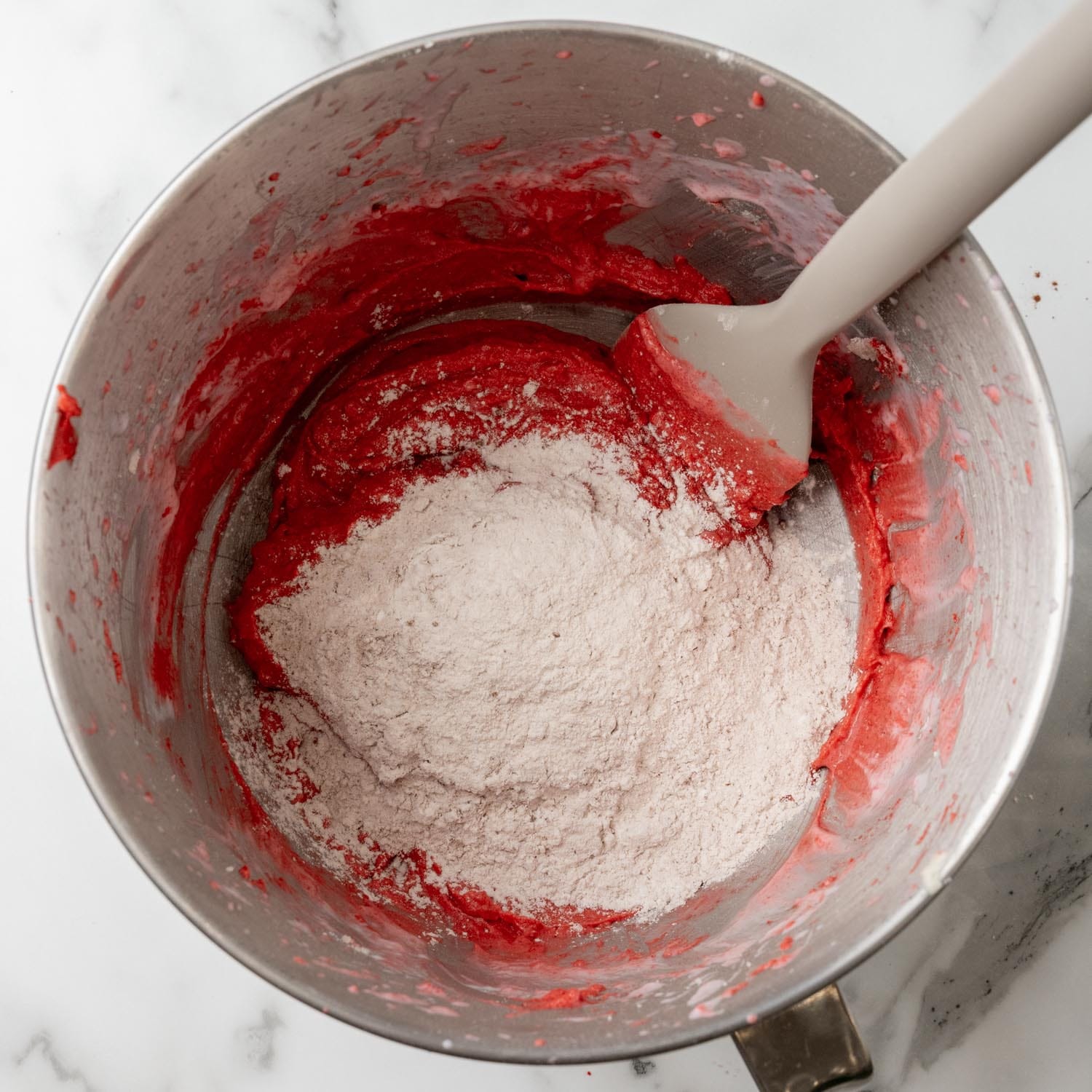 flour added to red velvet cake batter with a spatula in a metal mixing bowl.