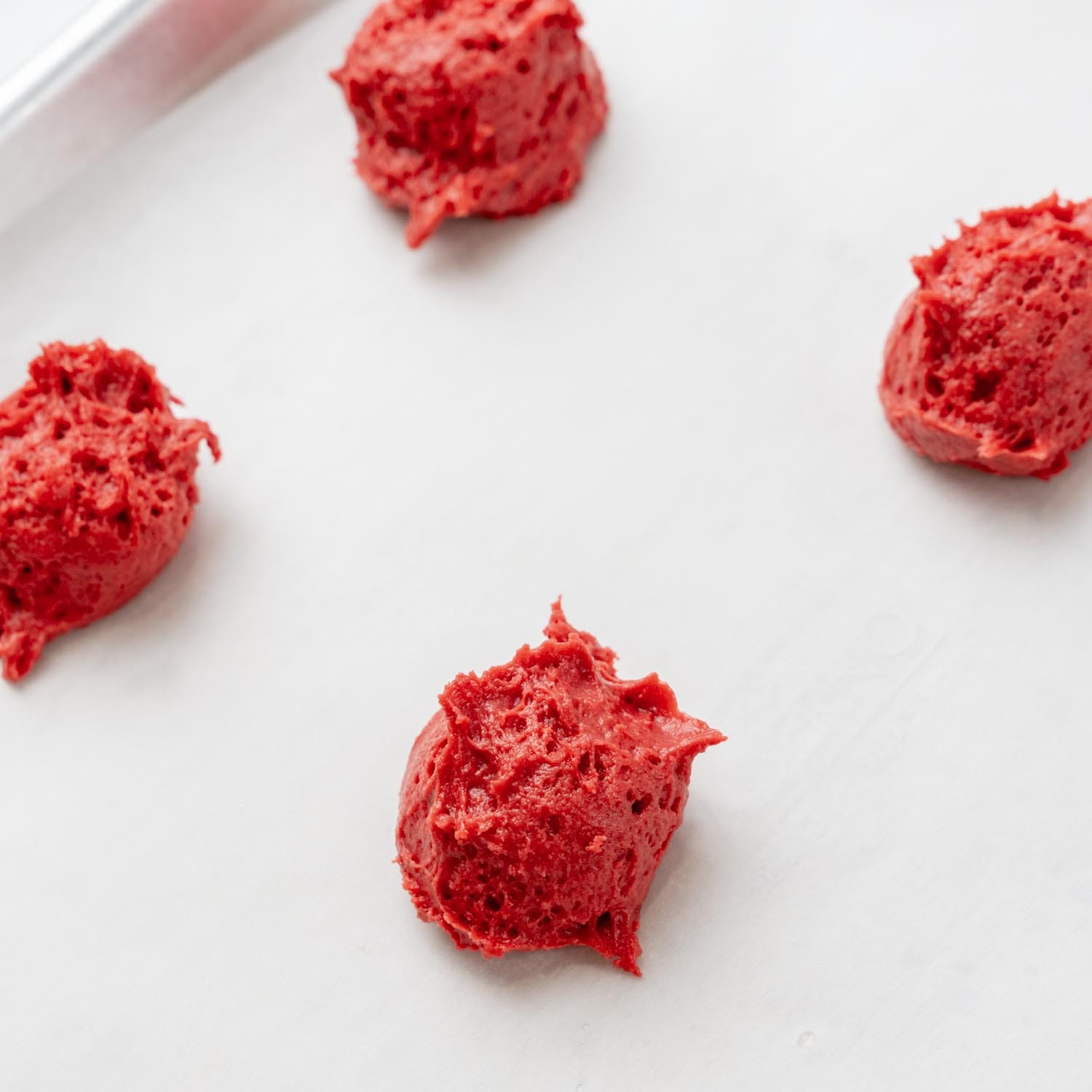 red velvet whoopie pie batter, in four round scoops on parchment paper.