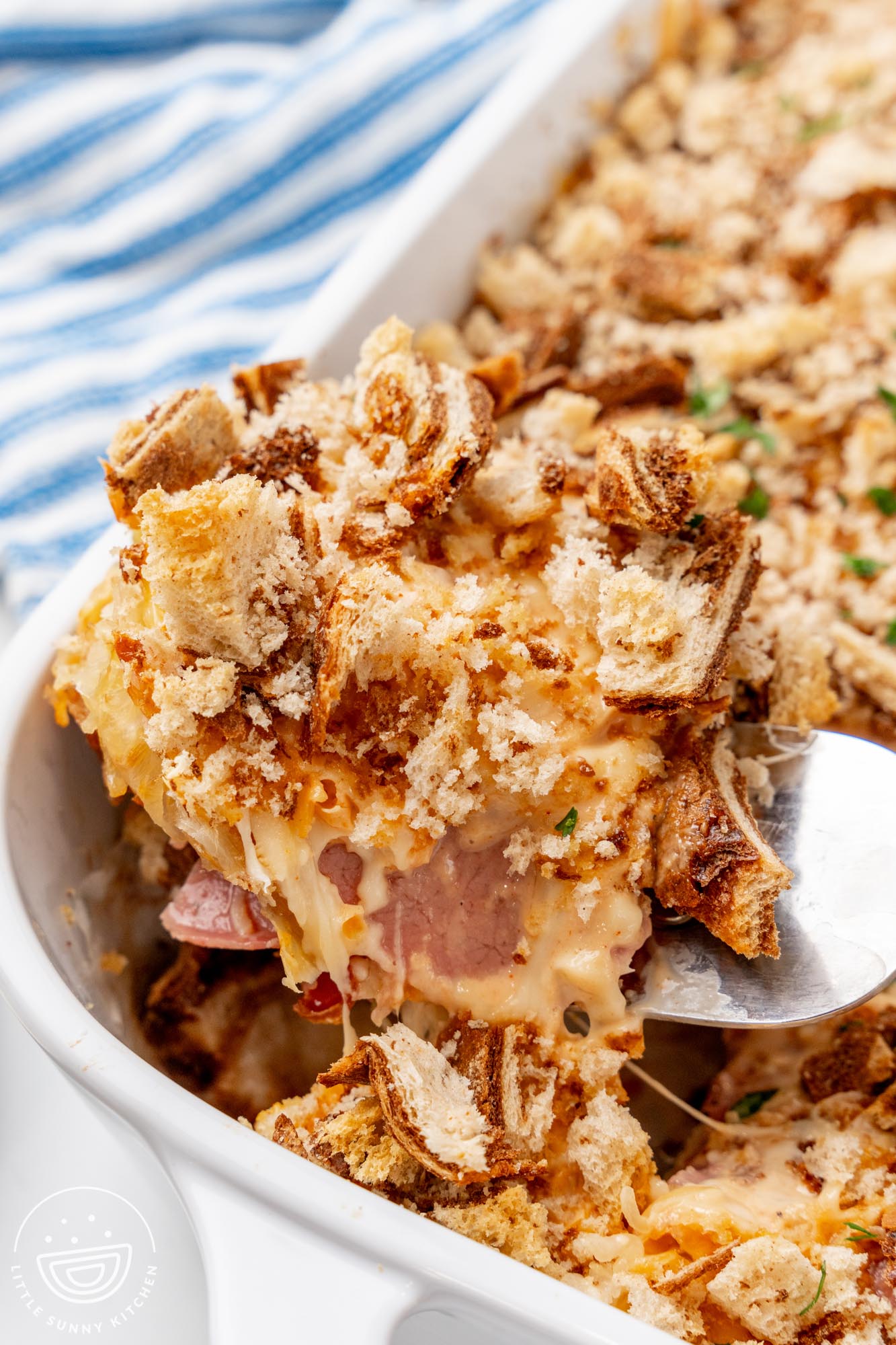 A spatula lifting a corner piece of homemade Reuben casserole with marble rye bread crumbs out of a white casserole dish.