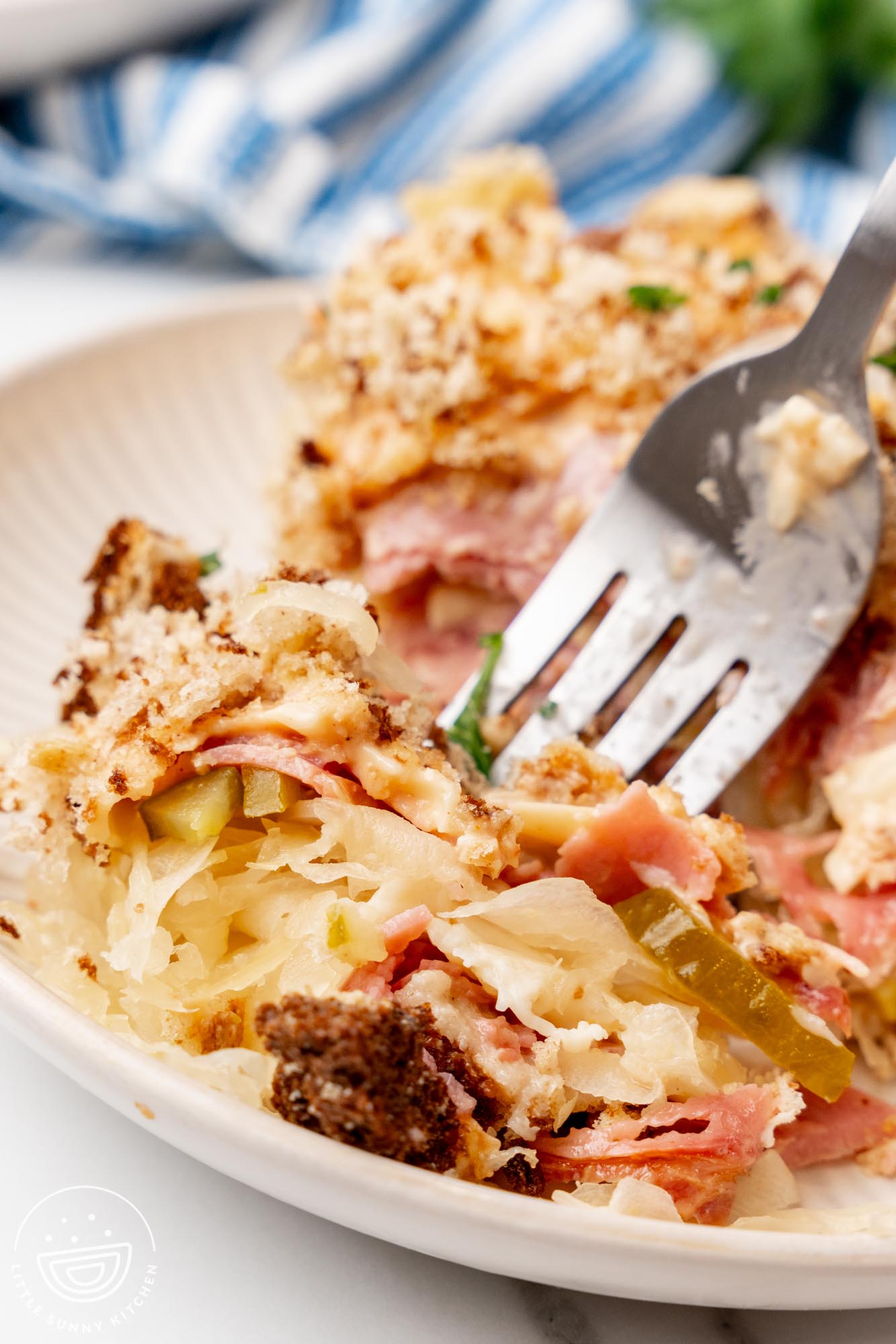 Closeup of a fork eating reuben casserole with sauerkraut, corned beef, and rye crumbs.