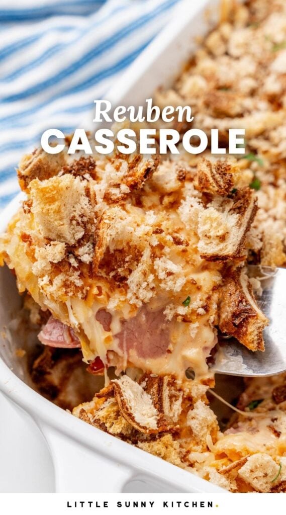 A spatula lifting a corner piece of homemade Reuben casserole with marble rye bread crumbs out of a white casserole dish. Text overlay says "Reuben Casserole"