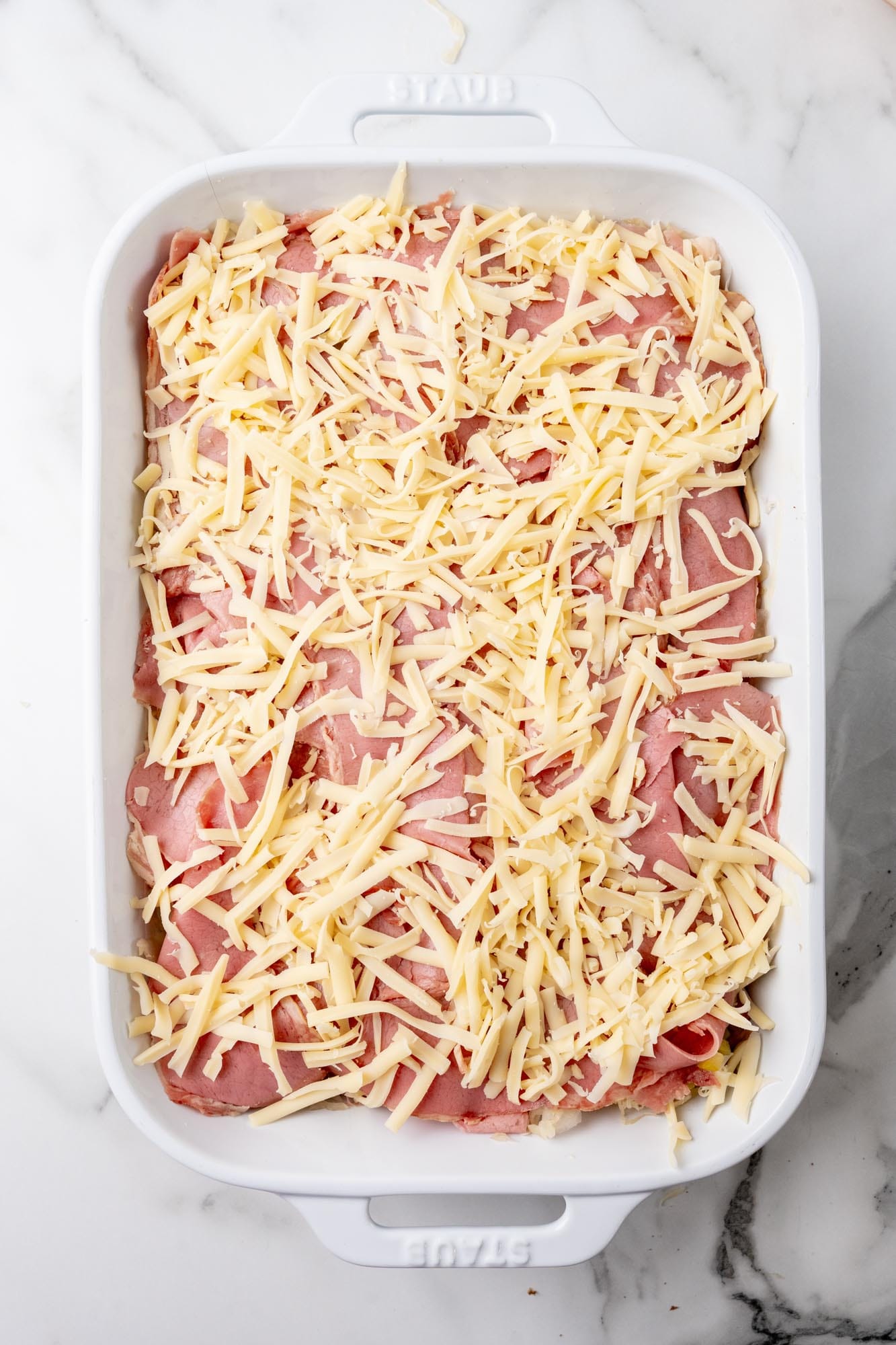 Layers of corned beef and shredded cheese in a white rectangular casserole dish.