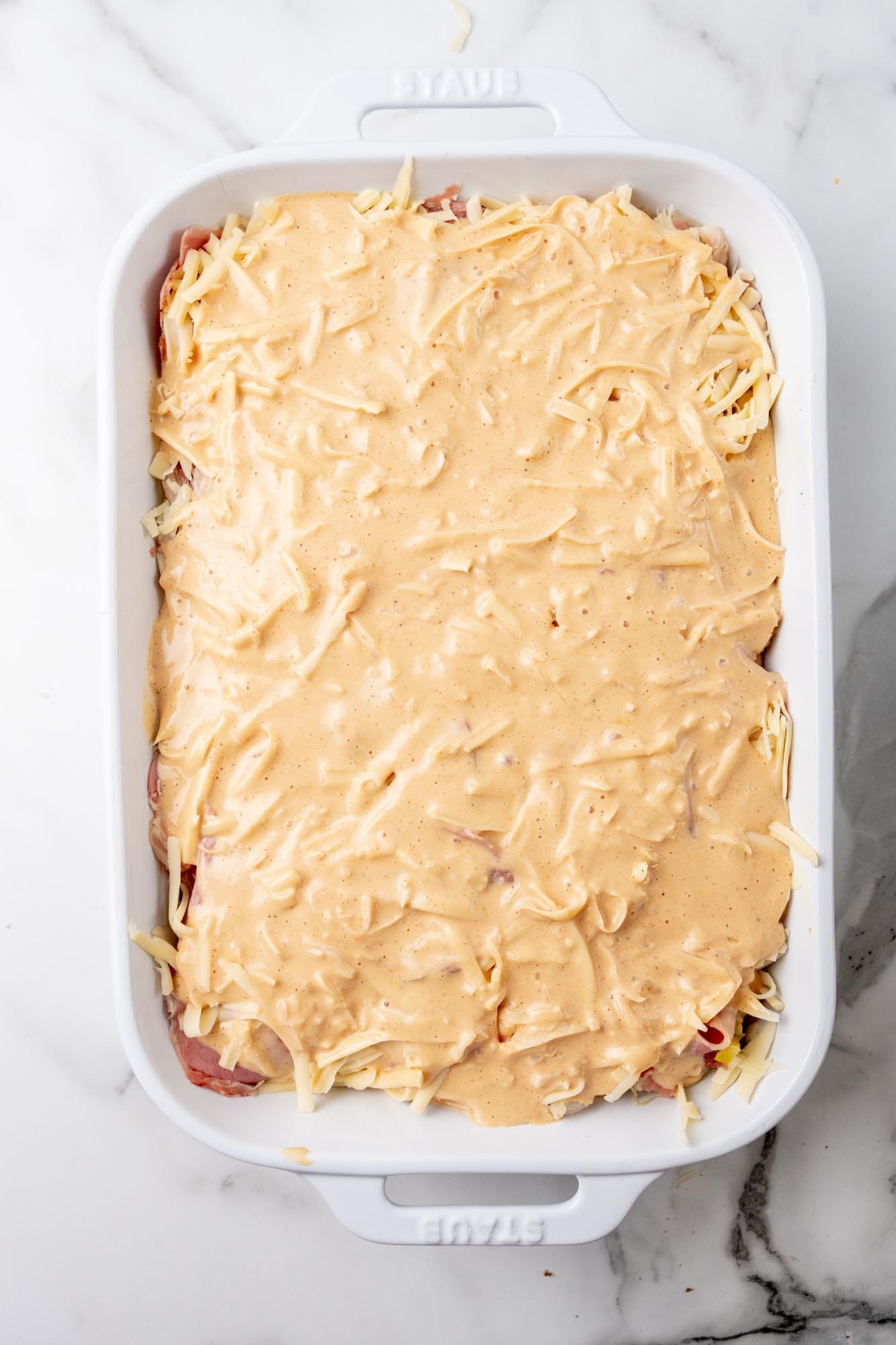 Reuben sauce poured over reuben casserole in a white ceramic pan.