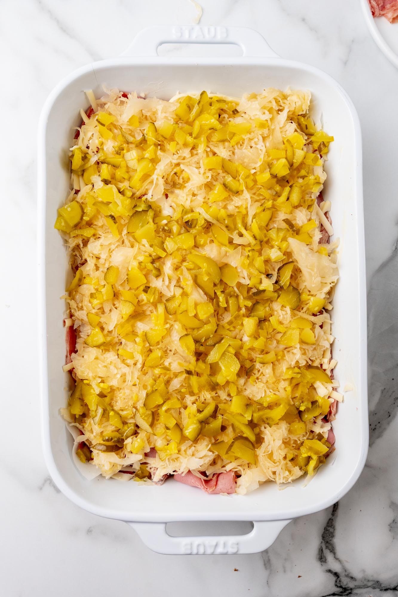 Chopped pickles and sauerkraut layered over corned beef and swiss to create reuben casserole in a 9x13 pan.