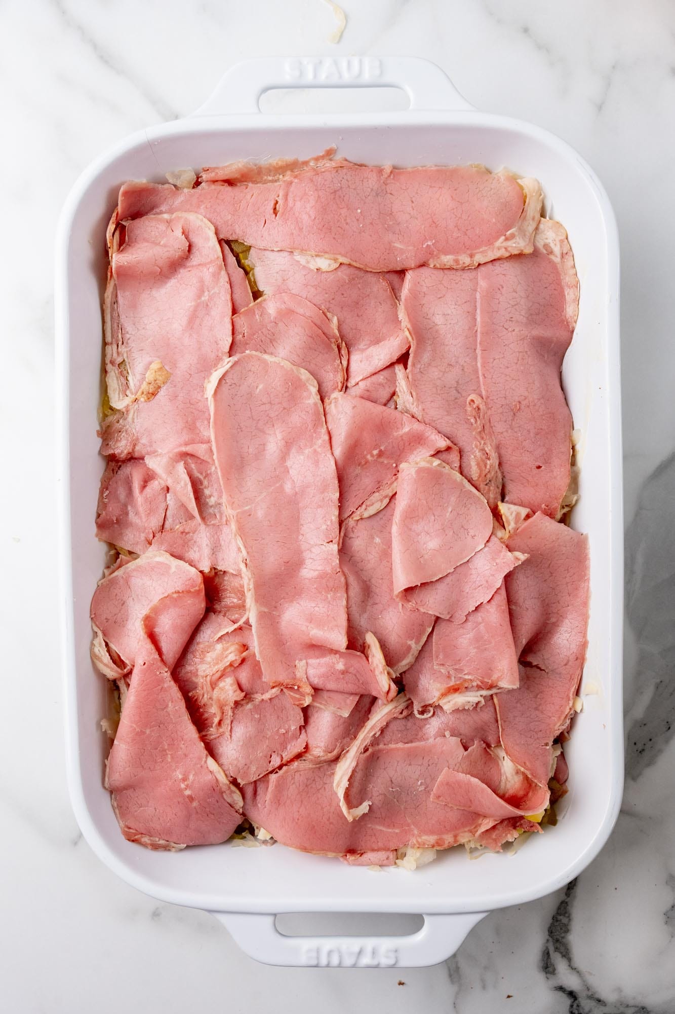 Slices of deli corned beef layered into a casserole dish.