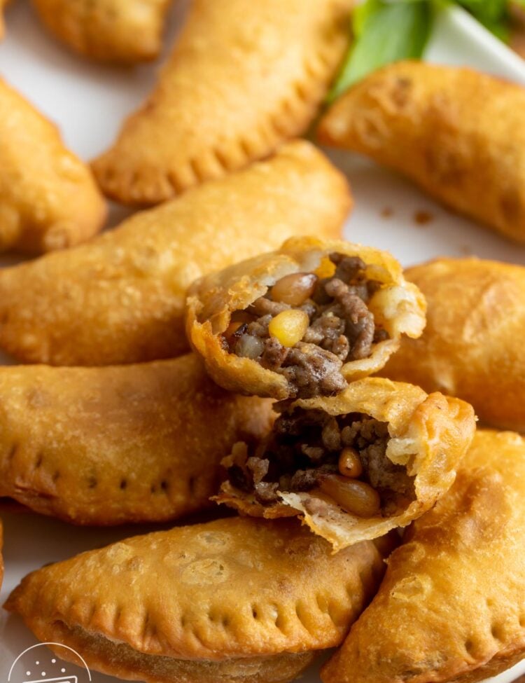 a platter of sambousek. One is split in half to show the ground beef and pine nut filling.