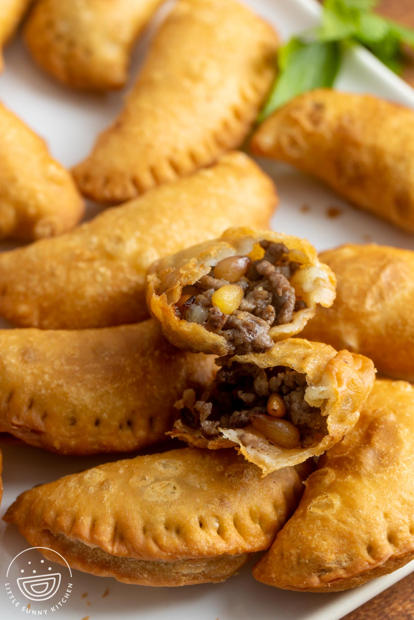 a platter of sambousek. One is split in half to show the ground beef and pine nut filling.