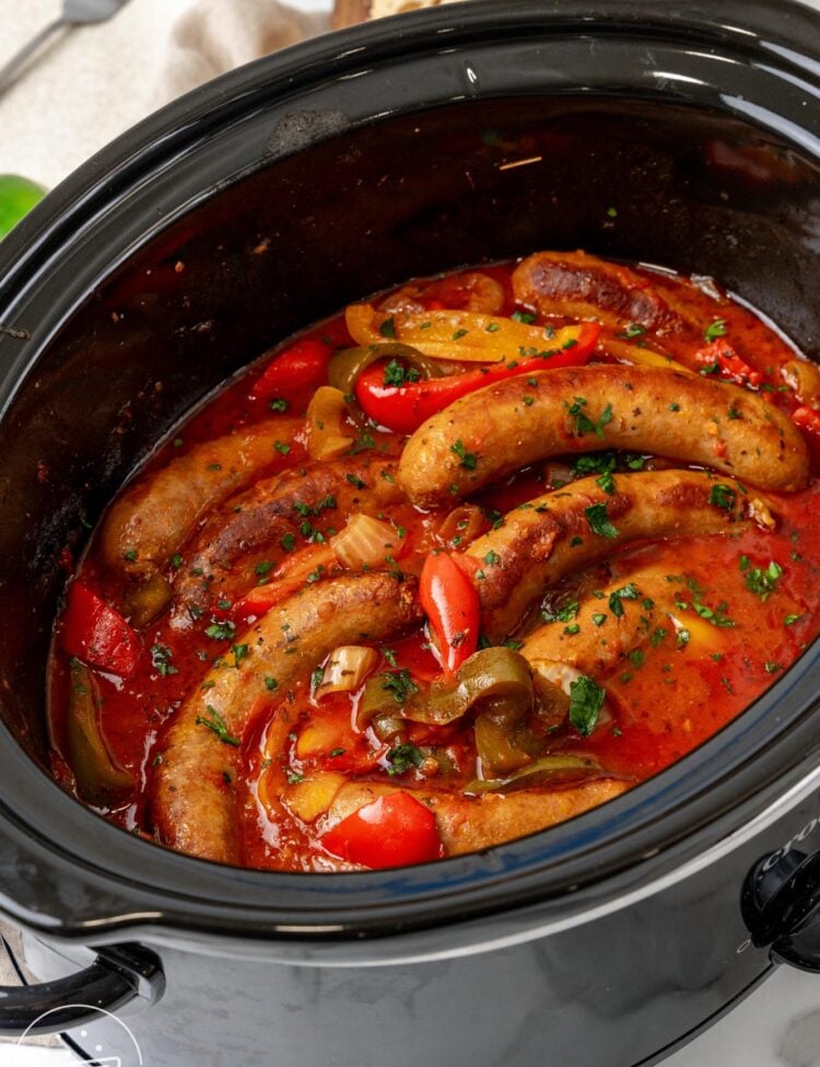 a black slow cooker filled with italian sausage and peppers.