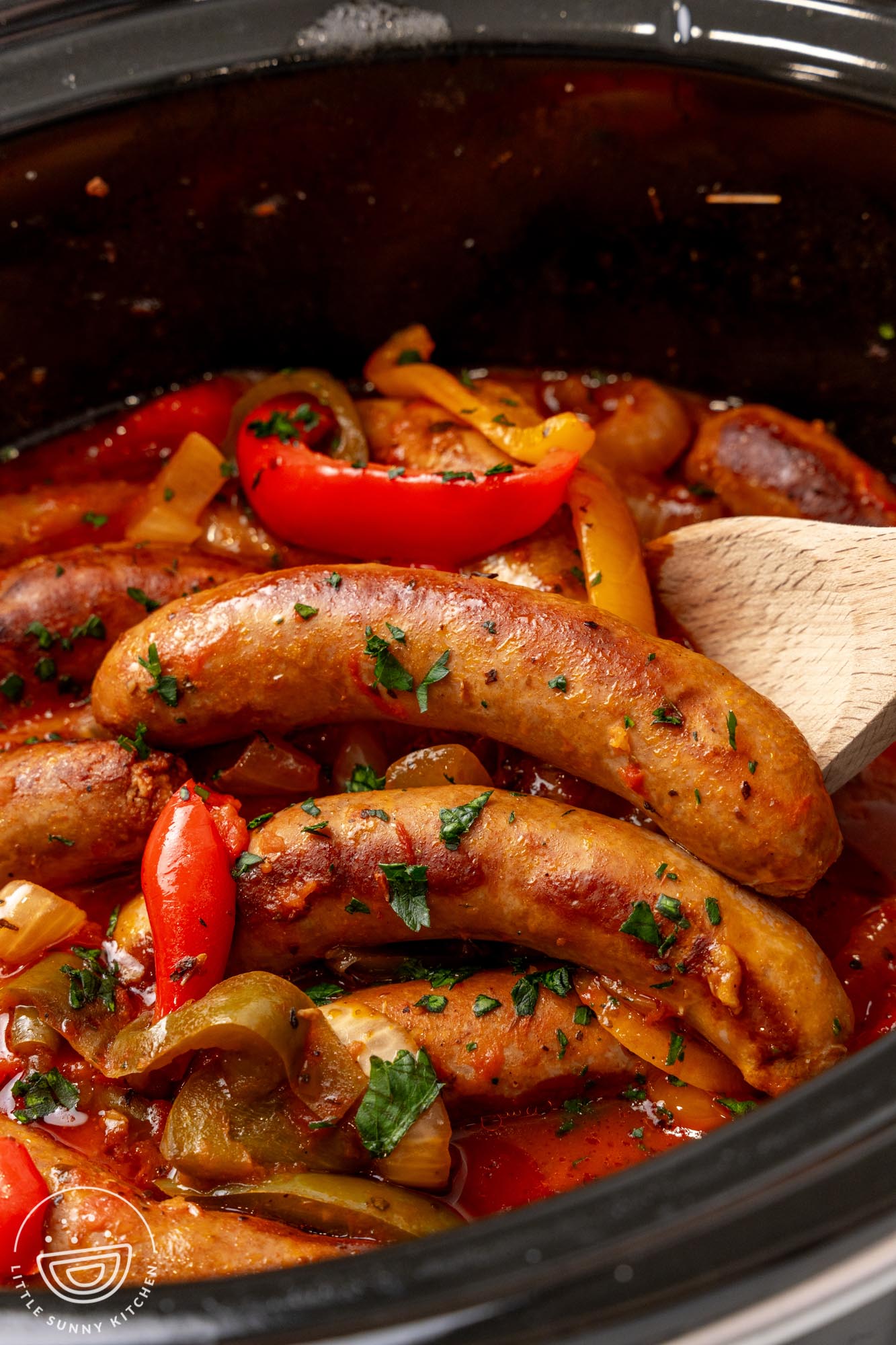 Italian sausage links in a black crock pot with braised peppers and onions.