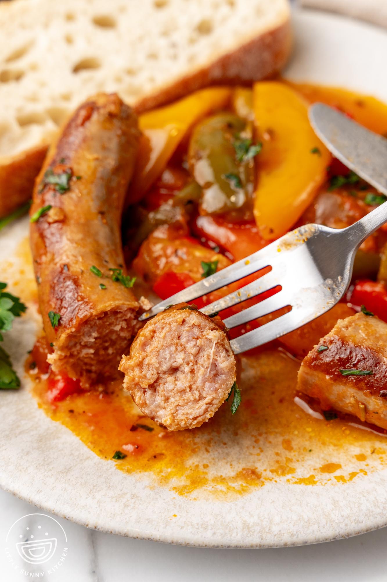 a plate of peppers and sausage. The sausage has been sliced and is picked up with a metal fork.