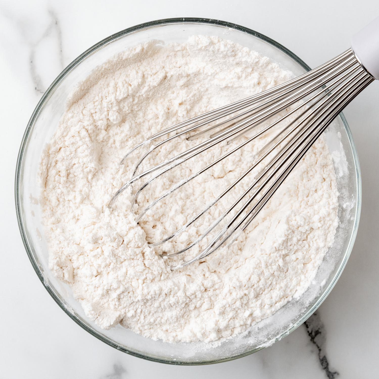 Flour whisked with other dry ingredients in a glass mixing bowl. 