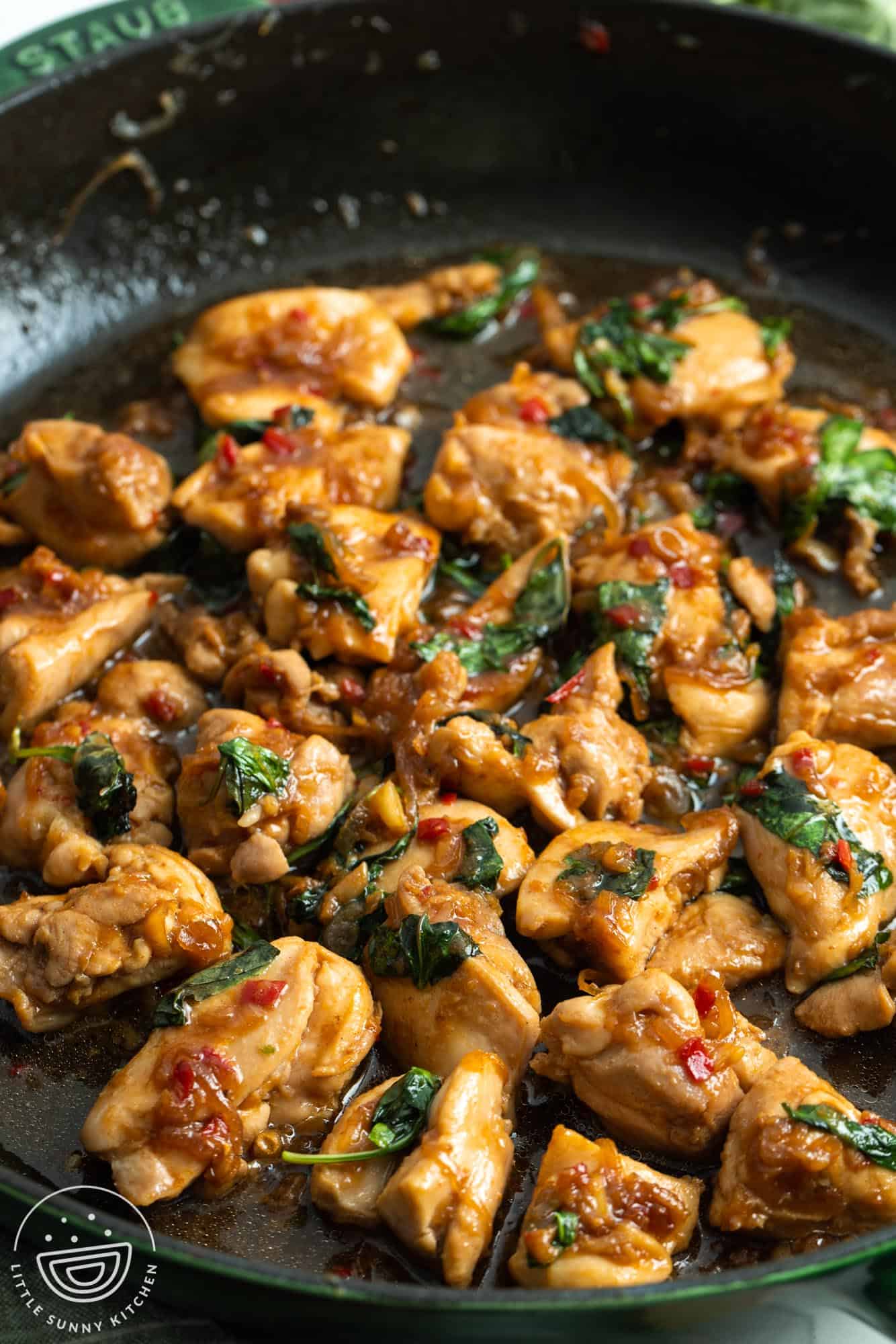 Cubed chicken thighs in a skillet with Thai basil and sauteed aromatics.